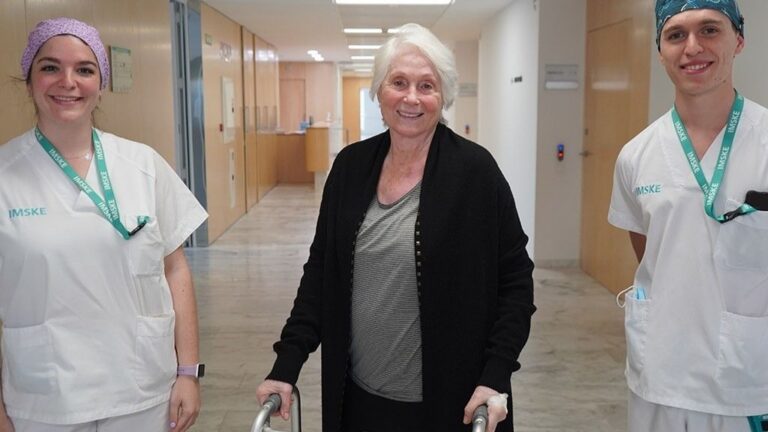 Pacient după o intervenție chirurgicală ortopedică mergând pe holul unui spital cu asistente medicale