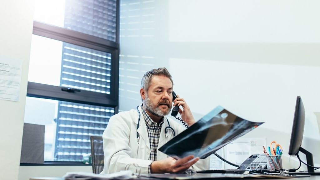 Medic expert care analizează o radiografie în timpul unei consultații telefonice privind a doua opinie medicală pentru un pacient care are în vedere o intervenție chirurgicală.